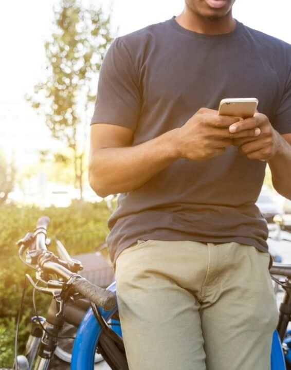 man holding smartphone leaning on bicycle during daytime