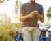 man holding smartphone leaning on bicycle during daytime