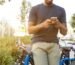 man holding smartphone leaning on bicycle during daytime